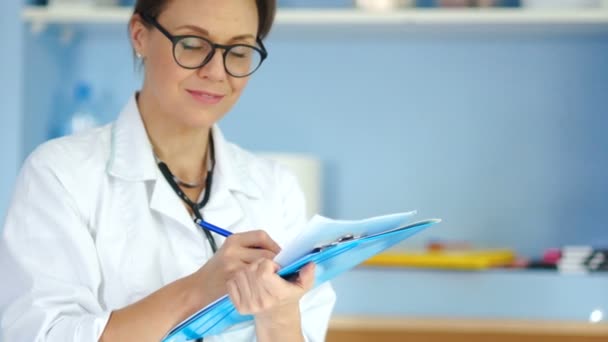 Lovely woman doctor in a white coat and glasses looks at the camera and smiles — Stock Video