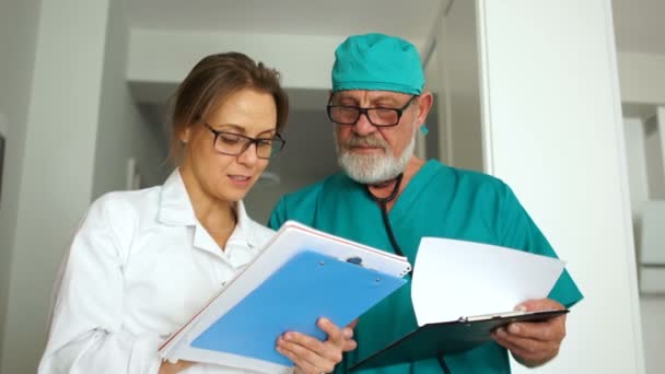 İş sırasında klinik personeli. Fotoğrafçıya poz verirken iki doktor. Gri saçlı, sakallı bir adam ve gözlüklü genç bir kadın. — Stok video