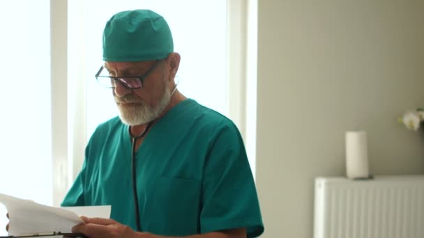 Gri sakallı ve gözlüklü olgun bir erkek doktor hastaların tıbbi geçmişini okur. Uluslararası Doktorlar Günü — Stok video