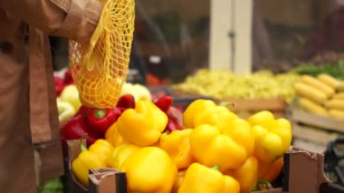 Kadın süpermarketten meyve alıyor, sarı güzel paprika. Sebzeleri tekrar kullanılabilir poşetlere koyar. Çevre ambalajı, sıfır atık, plastik, vejetaryen ve çiğ gıda diyetini durdurun