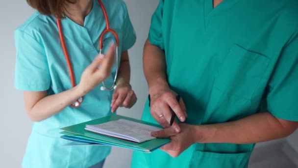 Närbild av läkare hand diskuterar patientbehandlingsplan. Man och kvinna i medicinska klänningar, med ett fonoskop, en mapp och en penna — Stockvideo