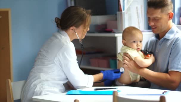 Père et son bébé à un rendez-vous chez le pédiatre. Une femme médecin examine un petit garçon d'un an et demi. Fête des pères — Video