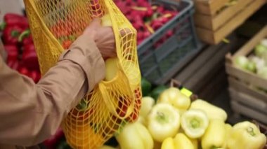 Yakın plan kimliği belirsiz kadın süpermarketten kırmızı biber alıyor. Müşteri sebzeleri tekrar kullanılabilir bir çantaya koyar, çevre dostu ambalajlar, plastikleri durdurur.