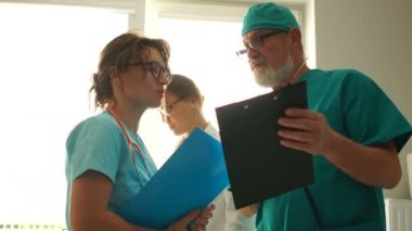 Doktor asistana talimat verir. Hastane odasında dikilirken konuşan yetişkin erkek ve genç kadın.