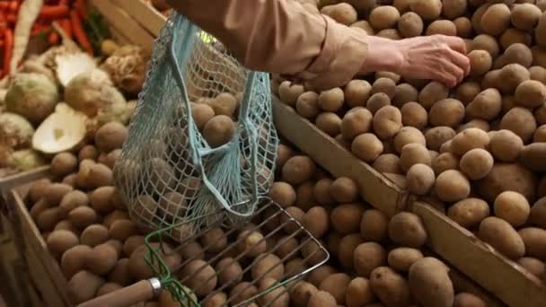 Женщина кладет руки в веревочный мешок новый картофель из деревянных коробок на рынке. Экологическая упаковка, ноль отходов — стоковое видео