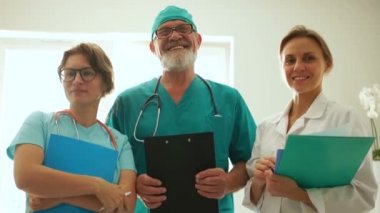 Beautiful portrait of doctors in medical suits. Mature man with a beard and two young female doctors smiling while looking at the camera