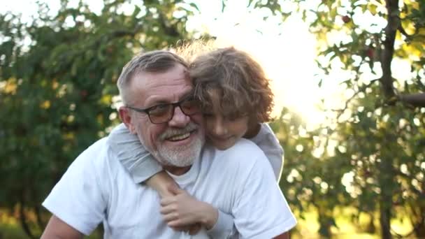 Los nietos felices abrazan al abuelo en el jardín. El niño vino a su abuelo y su hermano mayor — Vídeos de Stock