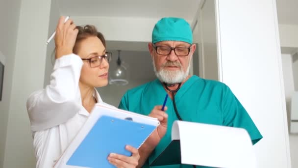 Mooi stel, twee dokters, een man en een vrouw, in medische jurken met mappen in hun handen, kijken in het frame en glimlachen. Internationale Dag van de artsen — Stockvideo