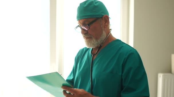 Volwassen mannelijke arts in groen medisch uniform lezen van een patiënt medische geschiedenis. Arts therapeut op een omweg in een ziekenhuis — Stockvideo