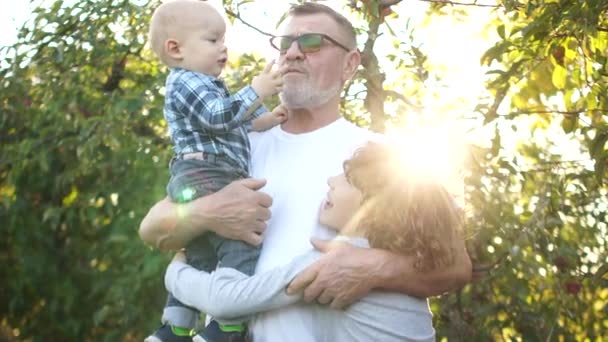 Feliz abuelo con dos nietos se divierte en el huerto de manzanas en otoño al atardecer — Vídeos de Stock