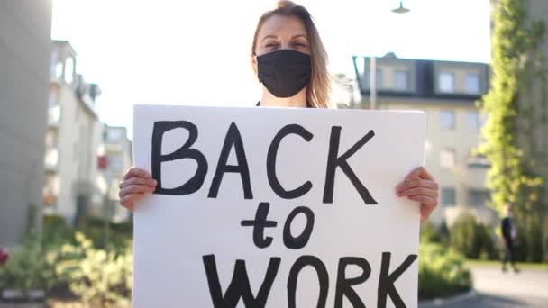 Flicka i svart skyddsmask protesterar mot stränga restriktiva åtgärder under karantänen av coronavirus covid-19. Flicka med affisch, porträtt på en solig dag — Stockvideo