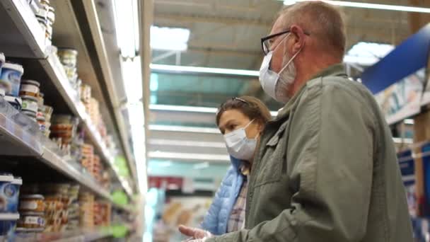 Marido e esposa selecionar produtos em uma prateleira em um supermercado e colocá-los em um carrinho de supermercado. Regras para visitar supermercados após quarentena coronavírus covid-19 . — Vídeo de Stock