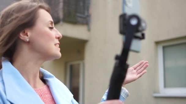 Fermecătoare femeie vlogger înregistrează video pentru blogul ei. Fata gestuează, ține un smartphone cu un stabilizator în fața ei — Videoclip de stoc
