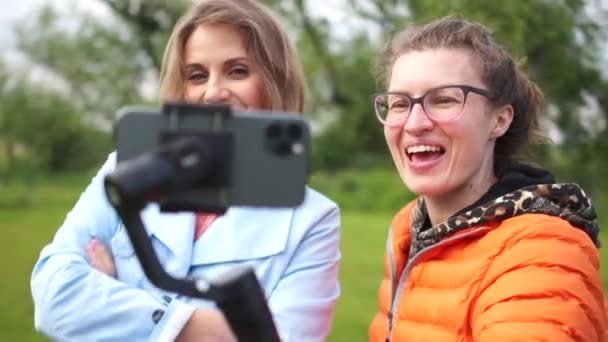 두 명의 젊은 여자 비디오 메이커. 두 젊은 여성 블로거가 스마트폰 카메라 앞에서 포즈를 취하고 있습니다. 여성들은 스마트폰 과 안정 화 장치를 사용하여 vlog 를 위한 비디오를 찍는다 — 비디오