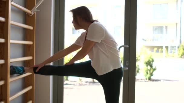 Sporty young woman exercising on gymnastic wall bars in fitness gym. Stretching exercises, regular sport — Stock Video