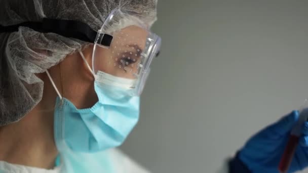 Retrato cercano de un técnico de laboratorio con traje protector y gafas. Diagnóstico de coronavirus covid-19. Reacción de PCR, pruebas ELISA para anticuerpos — Vídeo de stock