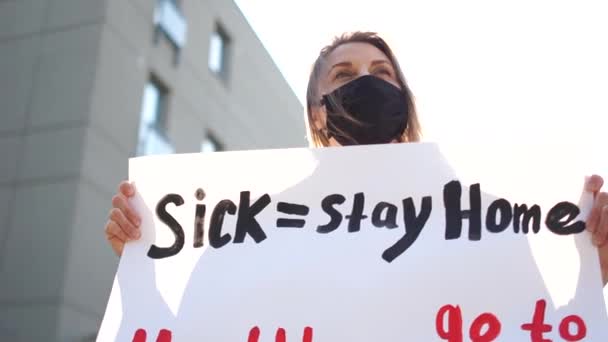 Sick - stay home healthy - go to work. Sunny portrait of a masked girl with a poster against lockdown quarantine restrictions — Stock Video