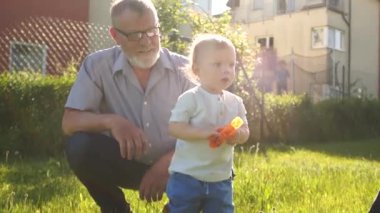 Büyükbaba ve torunun yakın portresi. Köyde güneşli bir gün, yaz tatili, bebek su sıçratıyor. Torun ve büyükbaba dışarıda eğleniyorlar. Babalar Günü