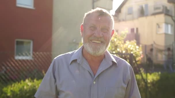 Idoso aposentado com um sorriso aberto e sincero, retrato próximo, conceito imobiliário. Um homem maduro com uma barba cinza está sorrindo enquanto olha para a câmera — Vídeo de Stock