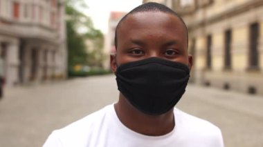 Sokakta siyah koruyucu maskeli gülümseyen Afro-Amerikan bir adamın portresi. Avrupa şehrinin genç öğrencisi, yeni normallik, karantina sonrası yaşam, Coronavirus covid-19