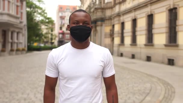 Portrait d'un jeune homme noir portant un masque noir dans une rue de la ville. Masque protecteur après quarantaine, vie post-quarantaine, nouvelle normalité, vie noire matière — Video