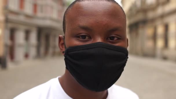Schwarzer zieht seine Maske ab. Porträt eines lächelnden afrikanisch-amerikanischen Mannes mit schwarzer Schutzmaske auf der Straße. Junge Studentin einer europäischen Stadt, nach der Quarantäne, Coronavirus covid-19 — Stockvideo