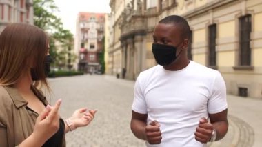 Erkek ve kız maskeli öğrenciler, karışık ırk çiftleri dans ediyor ve gülüyorlar. Mutlu çift Afrikalı adam ve beyaz kadın. Sokakta dans eden ırklar arası bir çift. Karantina sonrası yaşam
