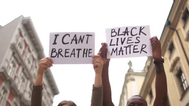 Ung blandet par studerende holder plakater med indskrift I KANT BREATHE og BLACK LIVES MATTER. Luk udendørs portræt. Hænderne op mod himlen i byen – Stock-video