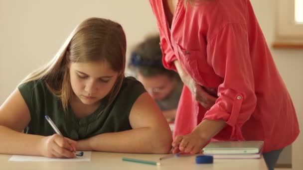 Children in the class write a final test. Teacher walks between the rows. Happy children with their teacher in classroom, doing schoolwork — Stock Video