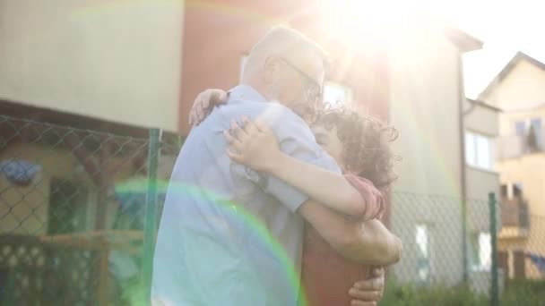 Oudere man en krullende tienerjongen. Gelukkige kleinzoon en grootvader knuffelend tegen de achtergrond van een huis in het dorp. Zonsondergang, zomervakantie, vaderdag — Stockvideo