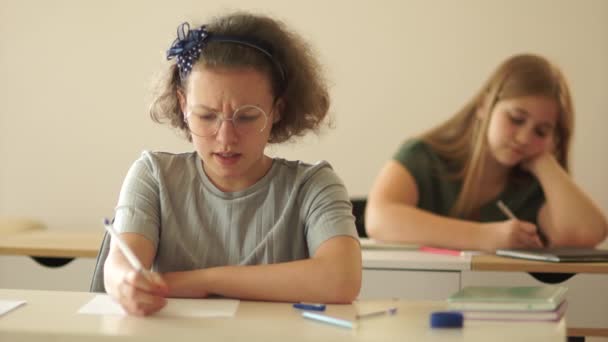 Gelukkige kinderen in de les. Een schoolmeisje schrijft een test, ze is moe en doet haar bril af en fronst. Terug naar school — Stockvideo