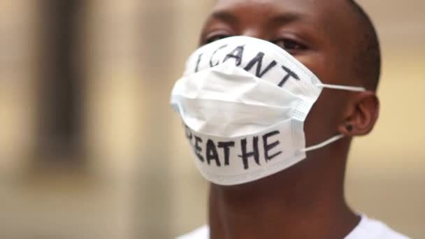 Zwarte levens doen ertoe, massale protesten tegen racisme in de VS en Europa. Outdoor portret van een Afro-Amerikaan in een medisch masker met de inscriptie Ik kan niet ademen — Stockvideo