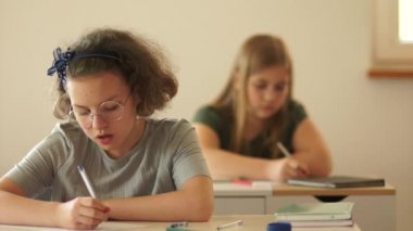 Dikte, final sınavı, liseli kızlar sınav yazıyor. Sınıftaki çocuklar masalarında oturuyorlar. Öğretmen satır aralarında yürür. Okula geri dön.