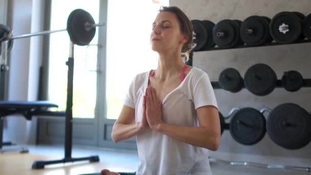 Menina medita na posição de lótus no ginásio após o treinamento. Relaxamento e relaxamento após o exercício, vida saudável, ioga e exercício — Vídeo de Stock