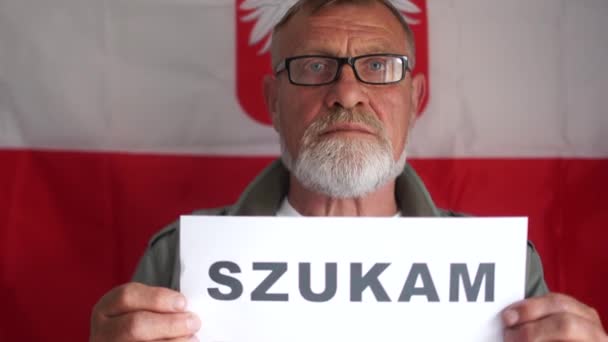 ポーランドの経済危機。ポーランド語の碑文を持つポスターを持つ男の肖像画は仕事が必要です。ポーランド国旗を背景にした成熟した男の肖像 — ストック動画