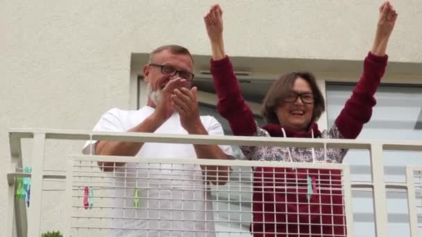 Marido y esposa mayores, familia aislada aplaudiendo en su balcón para apoyar al personal médico durante la pandemia mundial. Distancia social y autoaislamiento — Vídeo de stock
