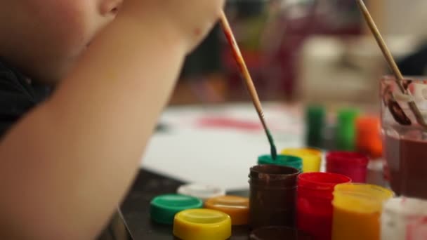 Retrato próximo, a criança desenha com uma escova e tinta vermelha, uma infância feliz, o desenvolvimento de habilidades e terapia de arte. Criança europeia bonito desenhando um quadro no jardim de infância — Vídeo de Stock