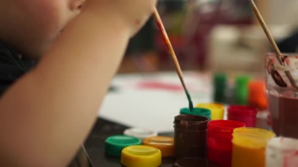 Retrato cercano, el niño dibuja con un pincel y pintura roja, una infancia feliz, el desarrollo de habilidades y terapia de arte. Lindo niño europeo dibujando un cuadro en el jardín de infantes — Vídeo de stock