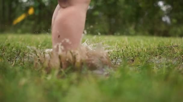 Een kind dat veel plezier heeft in een modderpoel. Clouse up portret van peuters blote voeten, een kind springen in het gras door een plas, een gelukkige jeugd, veel plezier — Stockvideo