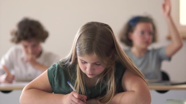 Os alunos sentam-se em suas mesas e escrevem em seus cadernos. O professor caminha pela sala de aula e ajuda os alunos. De volta à escola — Vídeo de Stock