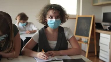 Kıvırcık maskeli kız elini kaldırdı, cevap vermeye hazırdı. Koronavirüs kovid 19 'dan sonra sınıftaki çocuklar karantina sonrası hayata, yeni normalliğe geri dönüyorlar.