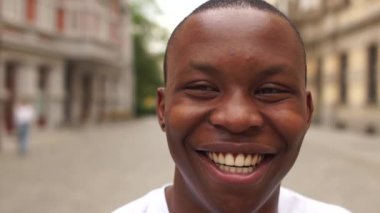 Şehir caddesinde beyaz tişörtlü genç bir Afro-Amerikan 'ın portresi. Siyah adam kameraya bakarken gülümsüyor.