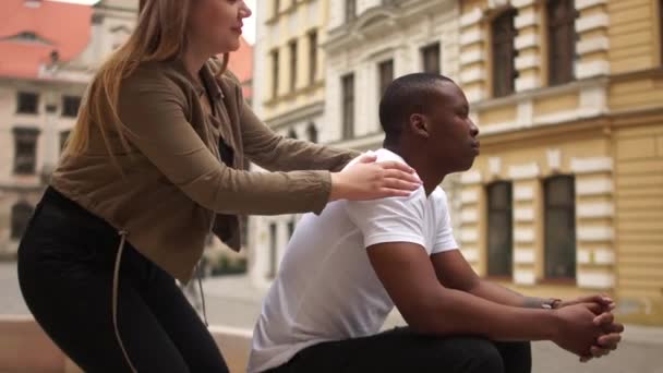 Una joven pareja mixta tiene una cita en la fuente. Chica blanca y chico negro se reunieron en la ciudad, Día de San Valentín — Vídeo de stock