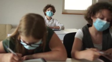 Koronavirüs kovid 19 'dan sonra sınıftaki çocuklar karantina sonrası okula dönüyorlar. Kıvırcık maskeli okul çocuğu cevap vermek için elini kaldırdı.