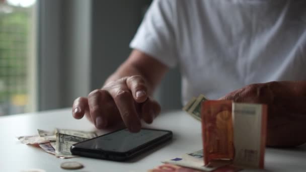 Um triste homem de barba cinza com óculos balança a cabeça, conta dinheiro usando uma calculadora em um smartphone. Crise financeira, queda do rendimento — Vídeo de Stock