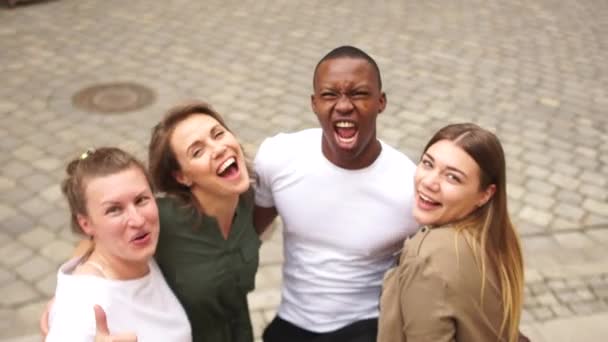 Giovani studenti di diverse nazionalità, un gruppo interrazziale di giovani, un ragazzo afroamericano e tre ragazze caucasiche che si abbracciano in una strada di città. Gruppo multietnico — Video Stock