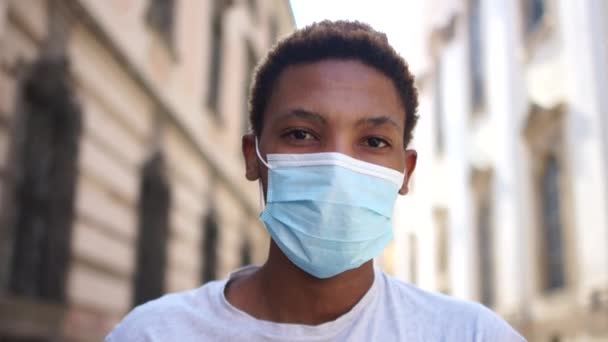 Svart man tar av sig masken. Porträtt av en leende afrikansk amerikan i svart skyddsmask på gatan. Ung student i en europeisk stad, efter karantänlivet, coronavirus covid-19 — Stockvideo