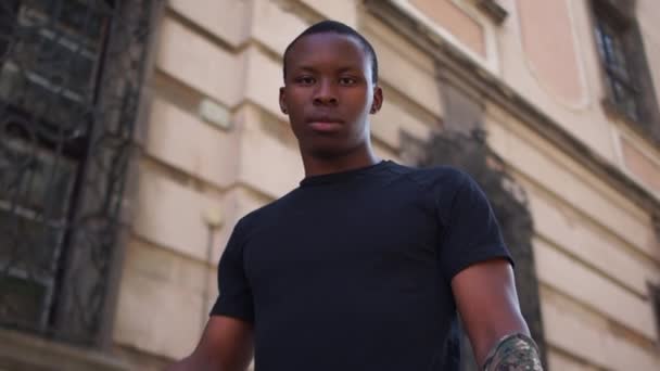 Utomhus skämmer bort en ung svart man i svart T-shirt. Afrikansk amerikansk student höjer knuten näve för att protestera mot rasism och våld — Stockvideo