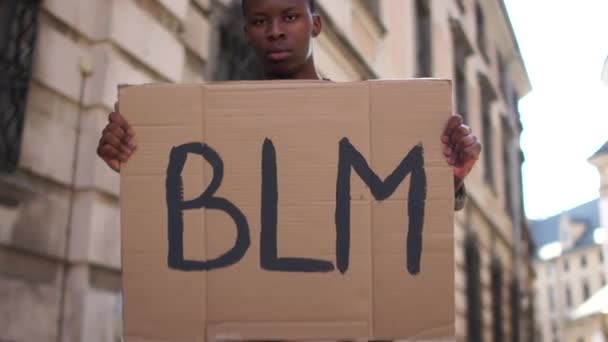 Uomo afroamericano con in mano un poster con la scritta BLM. L'azione di sostenere il movimento delle vite nere è importante. Proteste di massa negli Stati Uniti contro il razzismo e la violenza — Video Stock