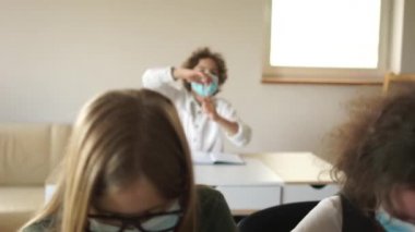 Sınıftaki çocuk elini kaldırdı ve öğretmenlerin sorularını cevaplamaya hazır. Koruyucu maskeli çocuklar okuldalar. Okula dönüyorum, kilitlendikten sonra öğreniyorum.